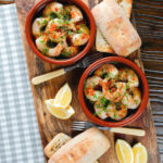 Overhead Spanish gambas (prawns) pil pil served with fresh parsley, bread and lemon wedges.