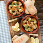 Overhead Spanish gambas (prawns) pil pil served with fresh parsley, bread and lemon wedges.