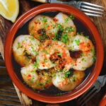 Close-up overhead Spanish gambas (prawns) pil pil served with fresh parsley, bread and lemon wedges.