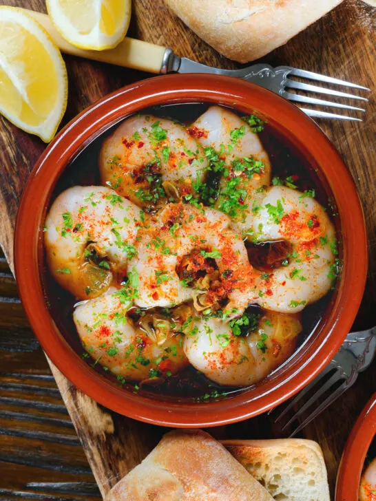 Close-up overhead Spanish gambas (prawns) pil pil served with fresh parsley, bread and lemon wedges.