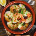 Close-up overhead Spanish gambas (prawns) pil pil served with fresh parsley, bread and lemon wedges.