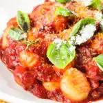 Close-up gnocchi in a red wine and tomato sauce served with basil and Parmesan.