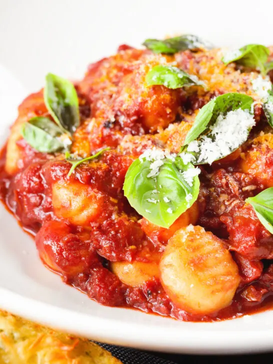 Close-up gnocchi in a red wine and tomato sauce served with basil and Parmesan.
