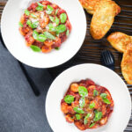 Overhead gnocchi in a red wine and tomato sauce served with basil, Parmesan and garlic bread.
