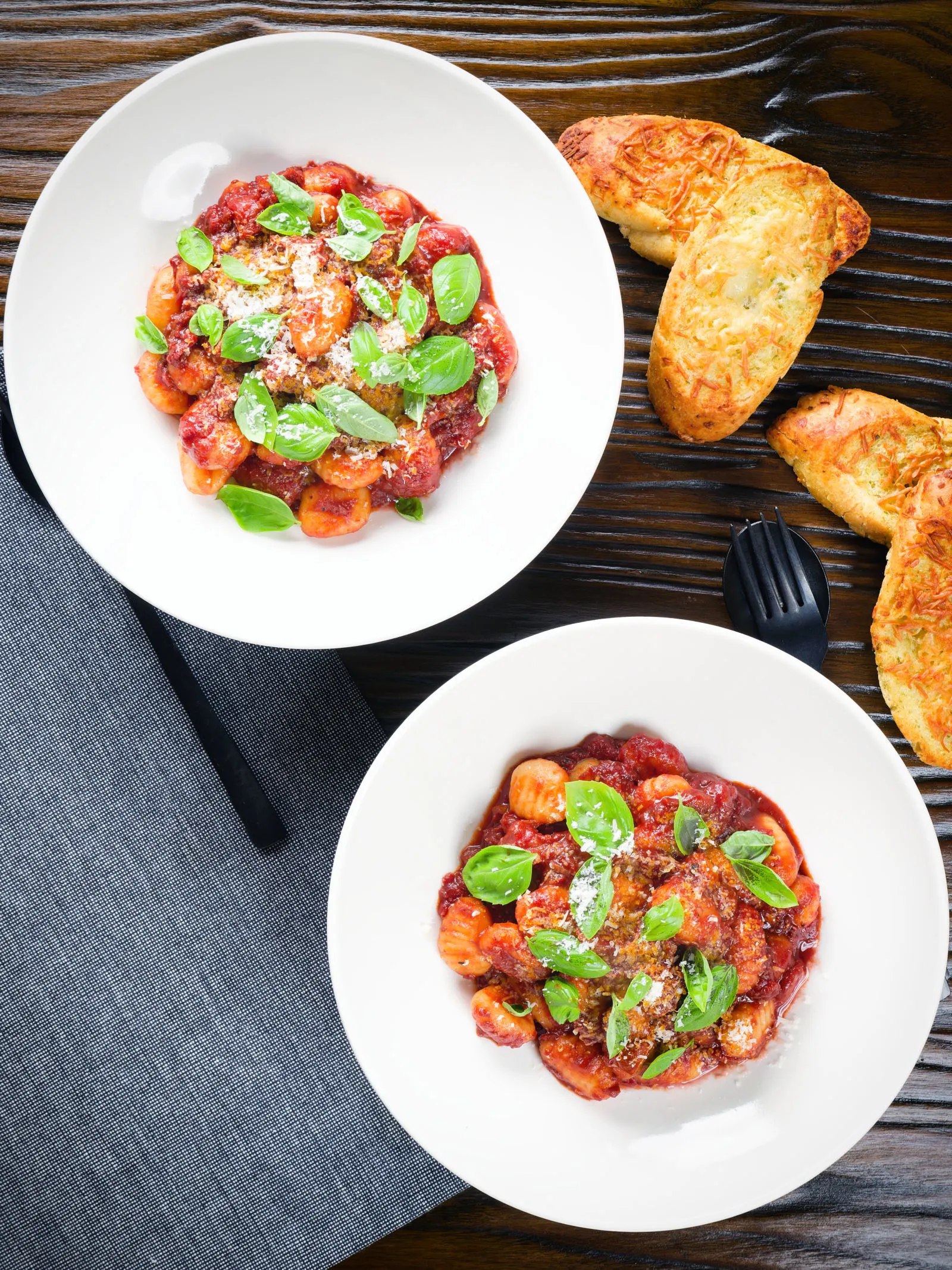 Overhead gnocchi in a red wine and tomato sauce served with basil, Parmesan and garlic bread.