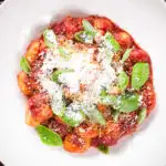 Close-up overhead gnocchi in a red wine and tomato sauce served with basil and Parmesan.