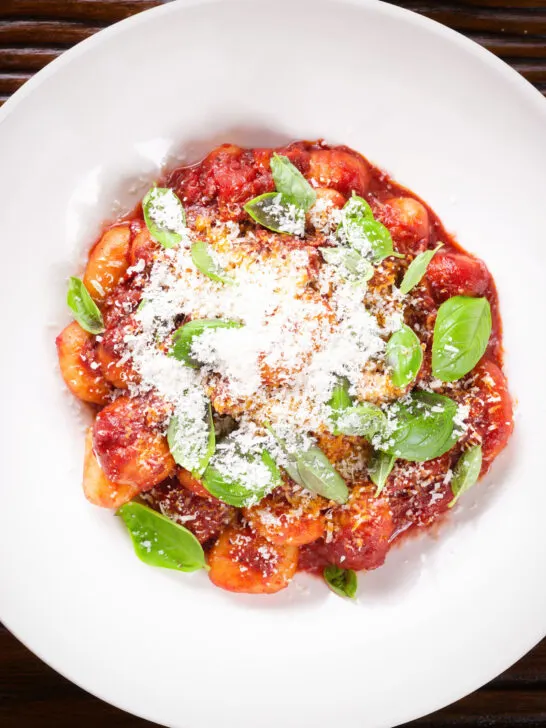 Close-up overhead gnocchi in a red wine and tomato sauce served with basil and Parmesan.