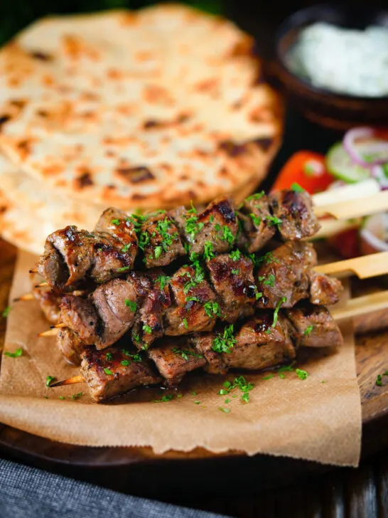 Lamb souvlaki skewers served with tzatziki, salad and pita flatbreads.