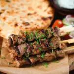 Lamb souvlaki skewers served with tzatziki, salad and pita flatbreads.