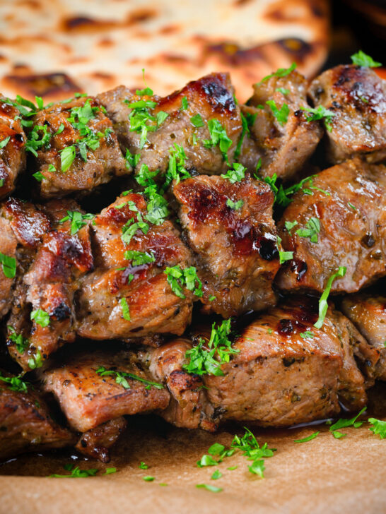 Close-up lamb souvlaki skewers served with Greek flatbreads.