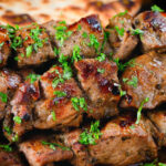 Close-up lamb souvlaki skewers served with Greek flatbreads.