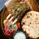 Overhead lamb souvlaki skewers served with tzatziki, salad and Greek flatbreads.