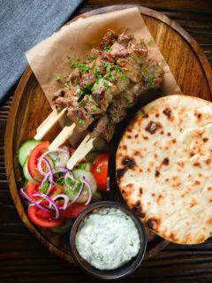 Overhead lamb souvlaki skewers served with tzatziki, salad and Greek flatbreads.