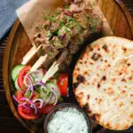 Overhead lamb souvlaki skewers served with tzatziki, salad and pita flatbreads.