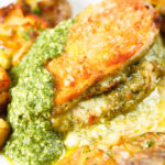 Close-up baked pesto and mozzarella stuffed chicken breast with crispy crushed potatoes.