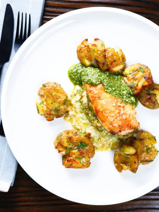 Overhead pesto and mozzarella stuffed chicken breast with crushed roasted new potatoes.