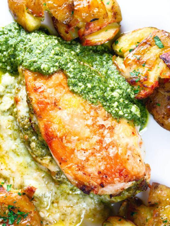 Overhead close-up baked pesto and mozzarella stuffed chicken breast with crispy crushed potatoes.