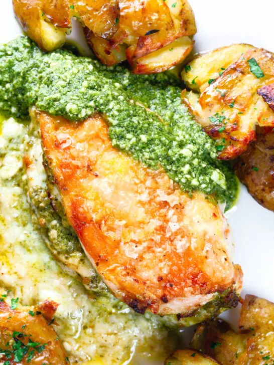 Overhead close-up baked pesto and mozzarella stuffed chicken breast with crispy crushed potatoes.