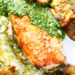Overhead close-up baked pesto and mozzarella stuffed chicken breast with crispy crushed potatoes.