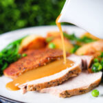 Cider gravy being poured over a serving of slow cooker pork loin.