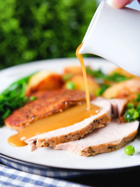 Cider gravy being poured over a serving of slow cooker pork loin.