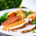 Cider gravy being poured over a serving of slow cooker pork loin.