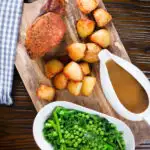 Overhead carved slow cooker pork loin, cider gravy, roast potatoes and green vegetables.