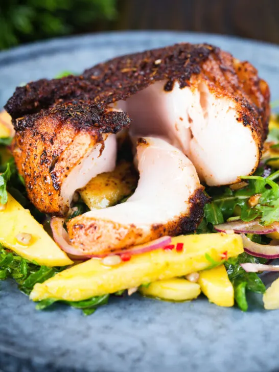 Cajun Blackened cod cut open showing white flaked fish served with mango salad.