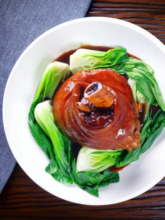 Overhead Chinese braised pork knuckle or shank served with steamed pak choi and braising juices.