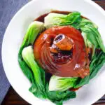 Overhead Chinese braised pork knuckle or shank served with steamed pak choi and braising juices.