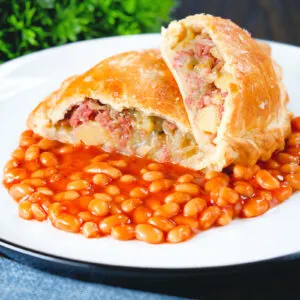 Homemade corned beef, onion and potato pasty cut open to show filling served with baked beans.