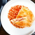 Overhead homemade corned beef, onion and potato pasty served with baked beans.