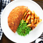 Overhead homemade minced beef filled crispy pancakes served with chips, peas and gravy.