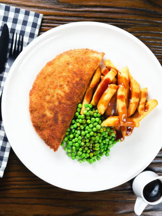 Overhead homemade minced beef filled crispy pancakes served with chips, peas and gravy.