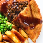Overhead close-up cut-open minced beef filled crispy pancakes served with chips, peas and gravy.