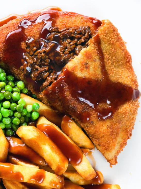 Overhead close-up cut-open minced beef filled crispy pancakes served with chips, peas and gravy.