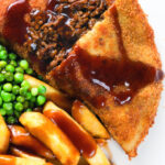 Overhead close-up cut-open minced beef filled crispy pancakes served with chips, peas and gravy.