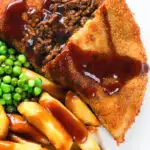 Overhead close-up cut-open minced beef filled crispy pancakes served with chips, peas and gravy.
