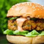 Close up fish burger with Thai flavours topped with sriracha mayonnaise and cucumber.