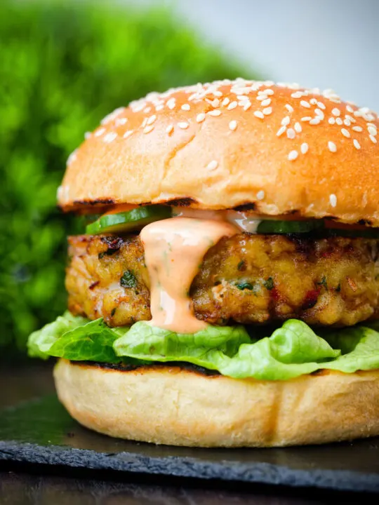 Close up fish burger with Thai flavours topped with sriracha mayonnaise and cucumber.