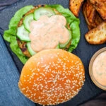 Overhead fish burger with Thai flavours topped with sriracha mayonnaise and cucumber.