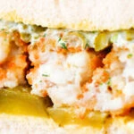 Detail shot of a fish finger sandwich with homemade tartar sauce and gherkins.