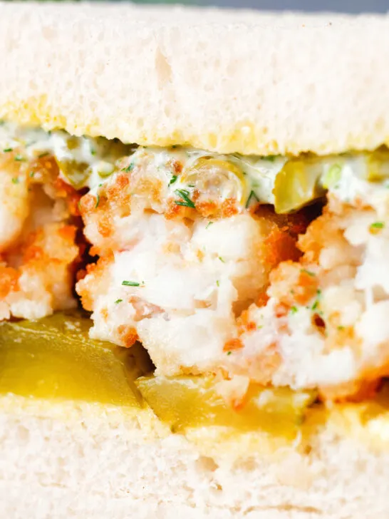 Detail shot of a fish finger sandwich with homemade tartar sauce and gherkins.