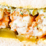Detail shot of a fish finger sandwich with homemade tartar sauce and gherkins.