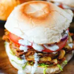 Bhaji burger or butty with lettuce, tomato, red onion and a mint raita sauce.