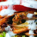 Close-up bhaji burger or butty with lettuce, tomato, red onion and a mint raita style sauce.