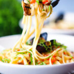 Mussels with pasta in butter and white wine with garlic, chilli and tomatoes on a fork.