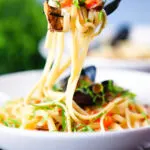 Mussels with pasta in butter and white wine with garlic, chilli and tomatoes on a fork.