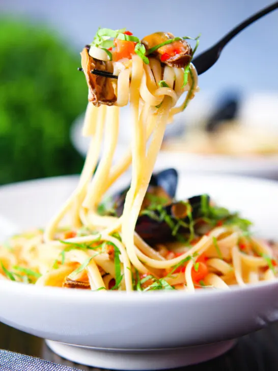 Mussels with pasta in butter and white wine with garlic, chilli and tomatoes on a fork.