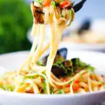 Mussels with pasta in butter and white wine with garlic, chilli and tomatoes on a fork.